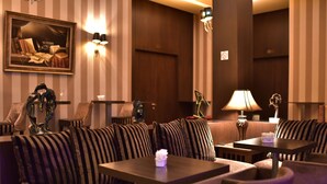 A cozy lounge area with striped sofas, a small table with a vase, and wall-mounted lamps. - Hotel Doro City (Tirana)