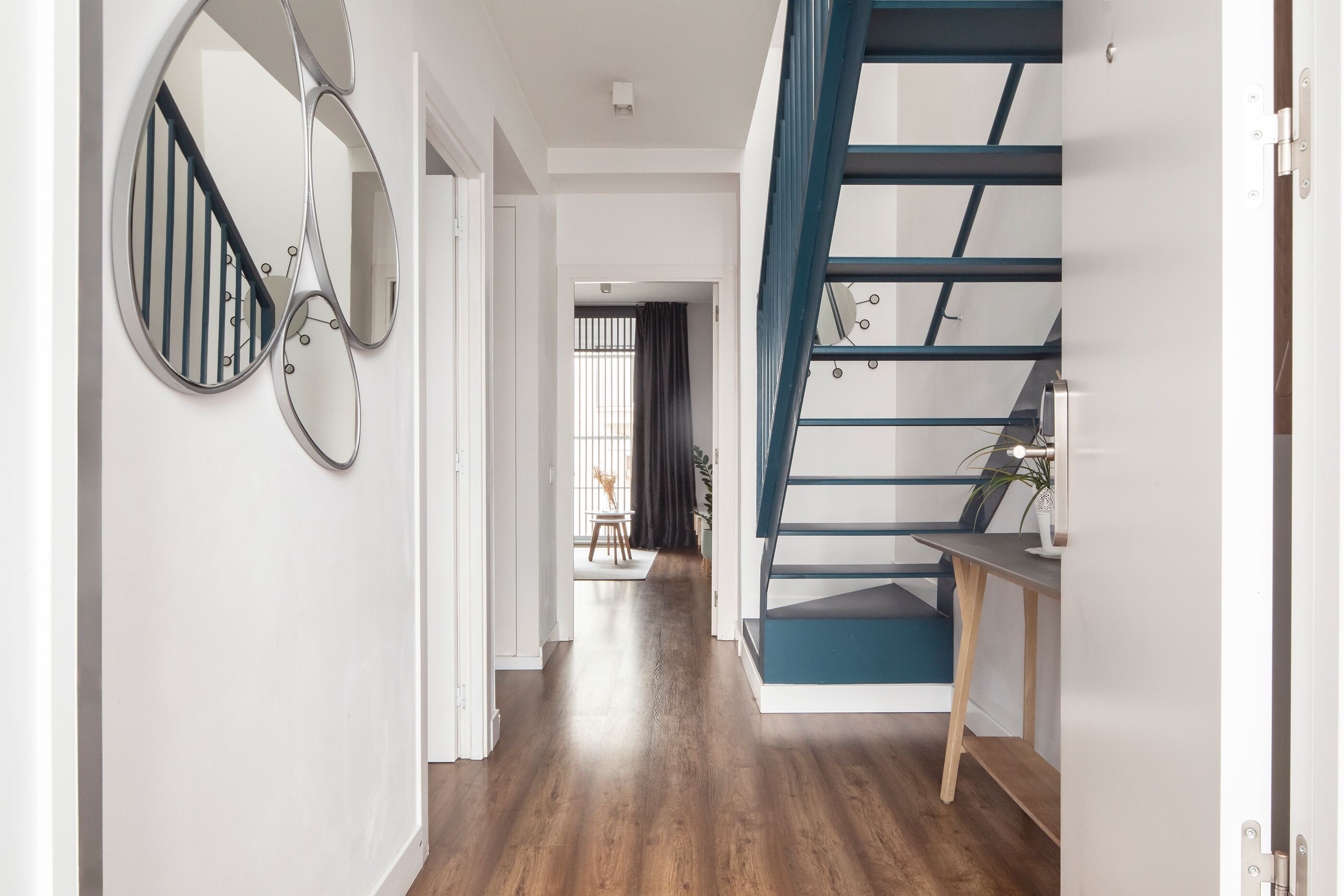 Een modern interieur met een houten vloer, een trap met blauwe accenten en een wandspiegel.
