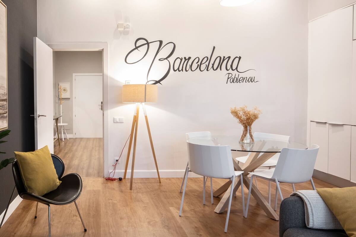 A modern dining area with a glass table, white chairs, and a wall-mounted lamp.