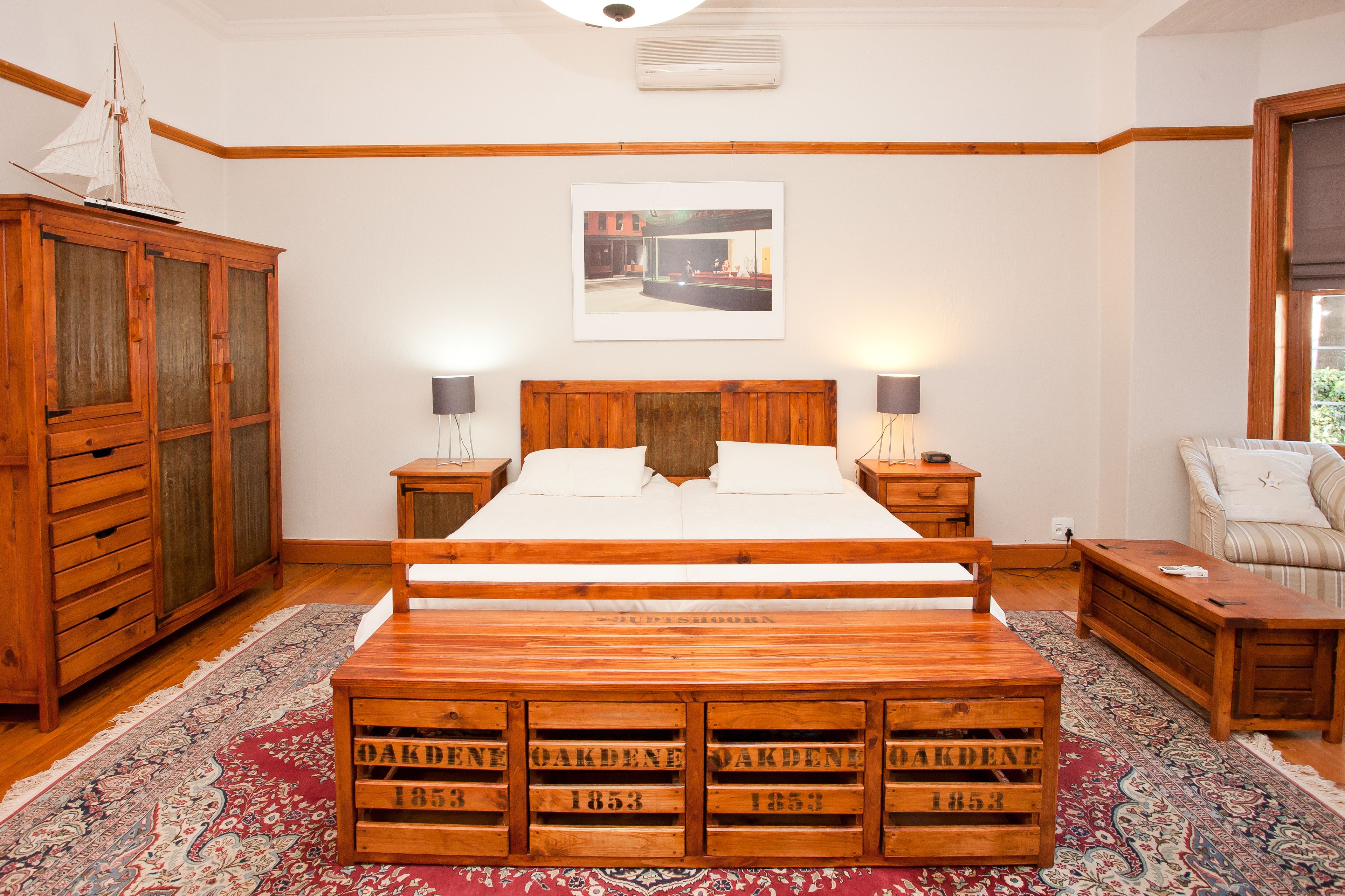 A bedroom with a wooden bed, nightstands, a wooden wardrobe, a bench with dates, and a rug.