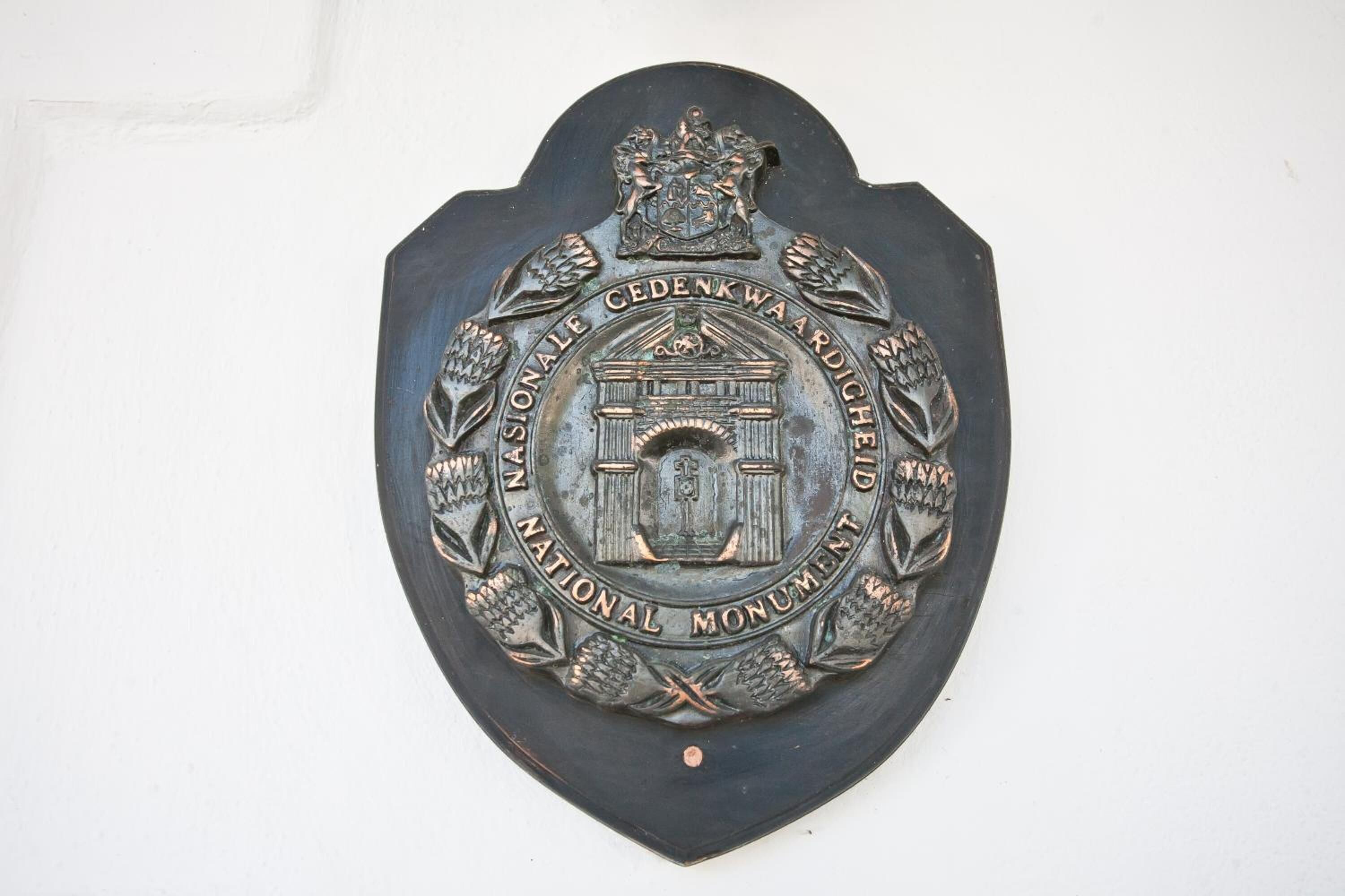 A metallic emblem with text and a central building design, mounted on a wall.