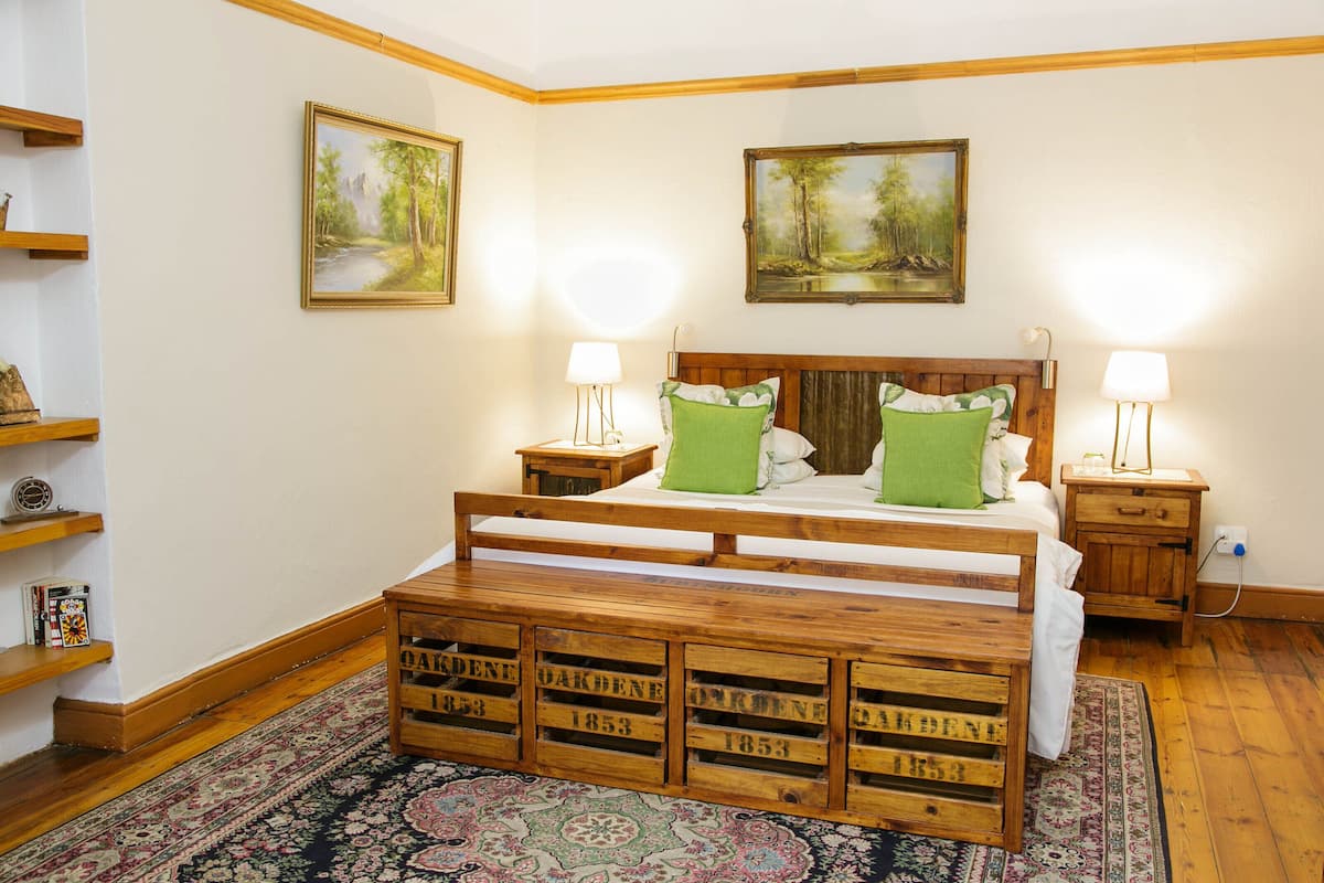 A bedroom with a wooden bed, two nightstands, green pillows, a wooden bench, and two paintings on the wall.