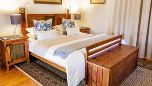 Una cama doble con cabecera de madera, dos mesitas de noche con lámparas, un banco al pie de la cama y dos cuadros enmarcados en la pared.