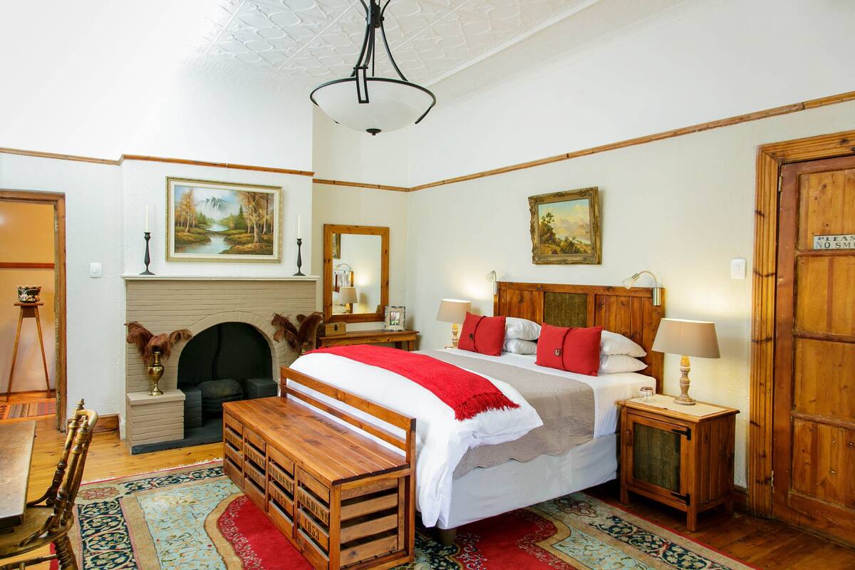 A bedroom with a bed, bedside tables, a wooden bench, a fireplace, and a large mirror.