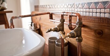 Un baño con tocador de madera, lavamanos blanco y tuberías de cobre.