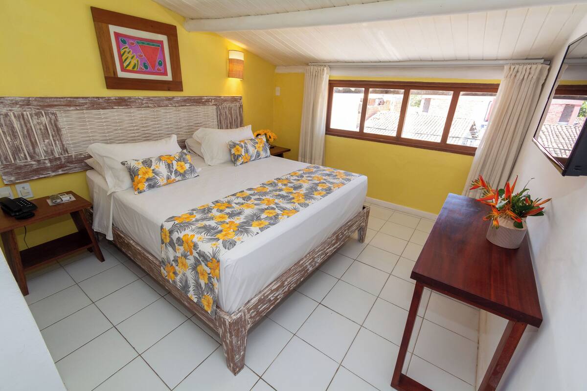 Un dormitorio con cama, mesitas de noche, cortinas en una ventana y un televisor de pared.