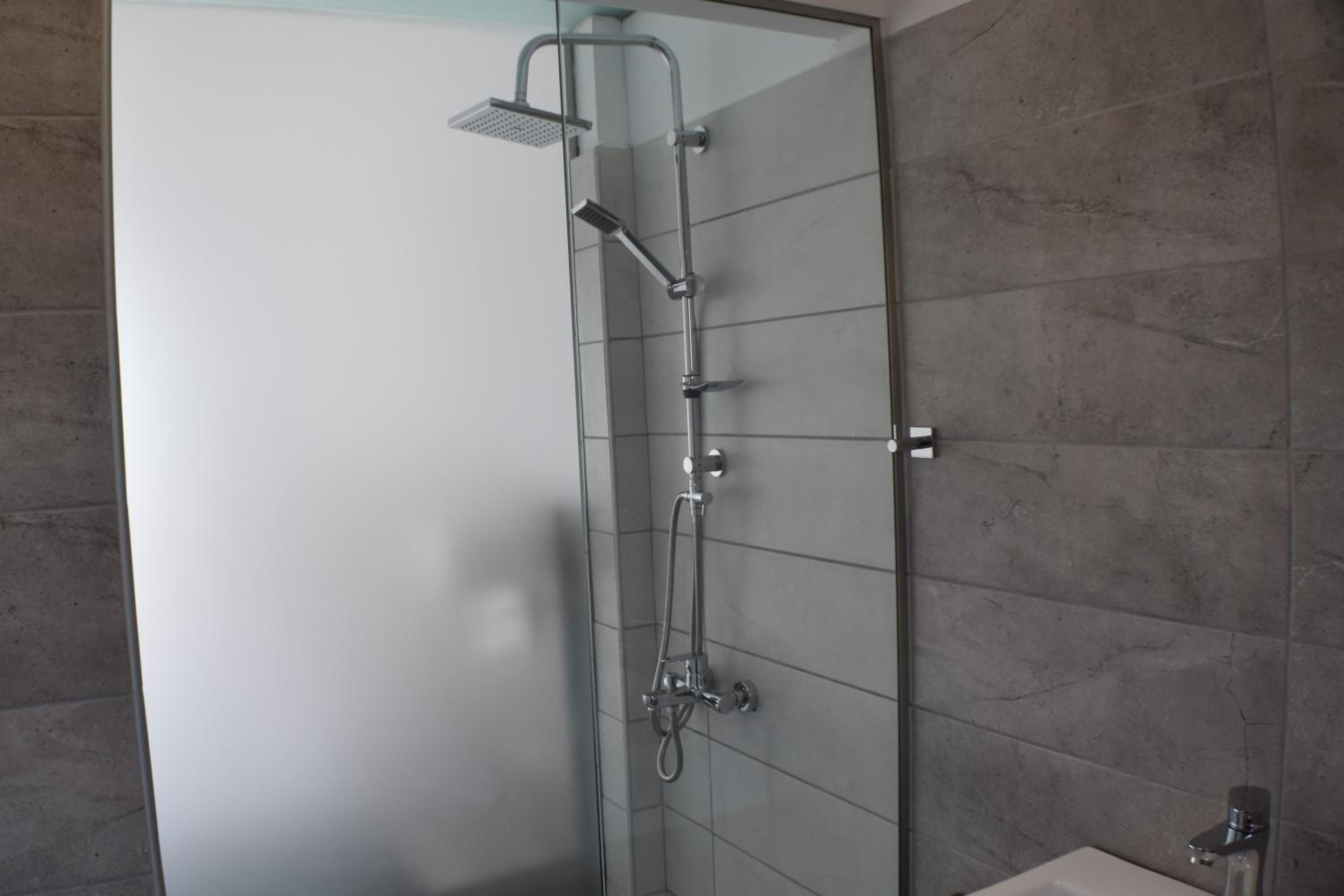Ducha envuelta en vidrio con cabezal de ducha manual e llave de pared.