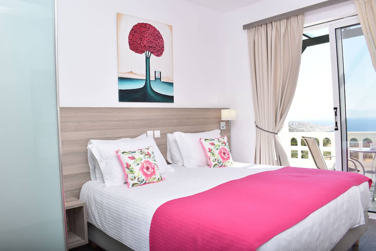 Habitación de hotel con una cama grande, un cuadro de un árbol en la pared y vistas al mar por la ventana.