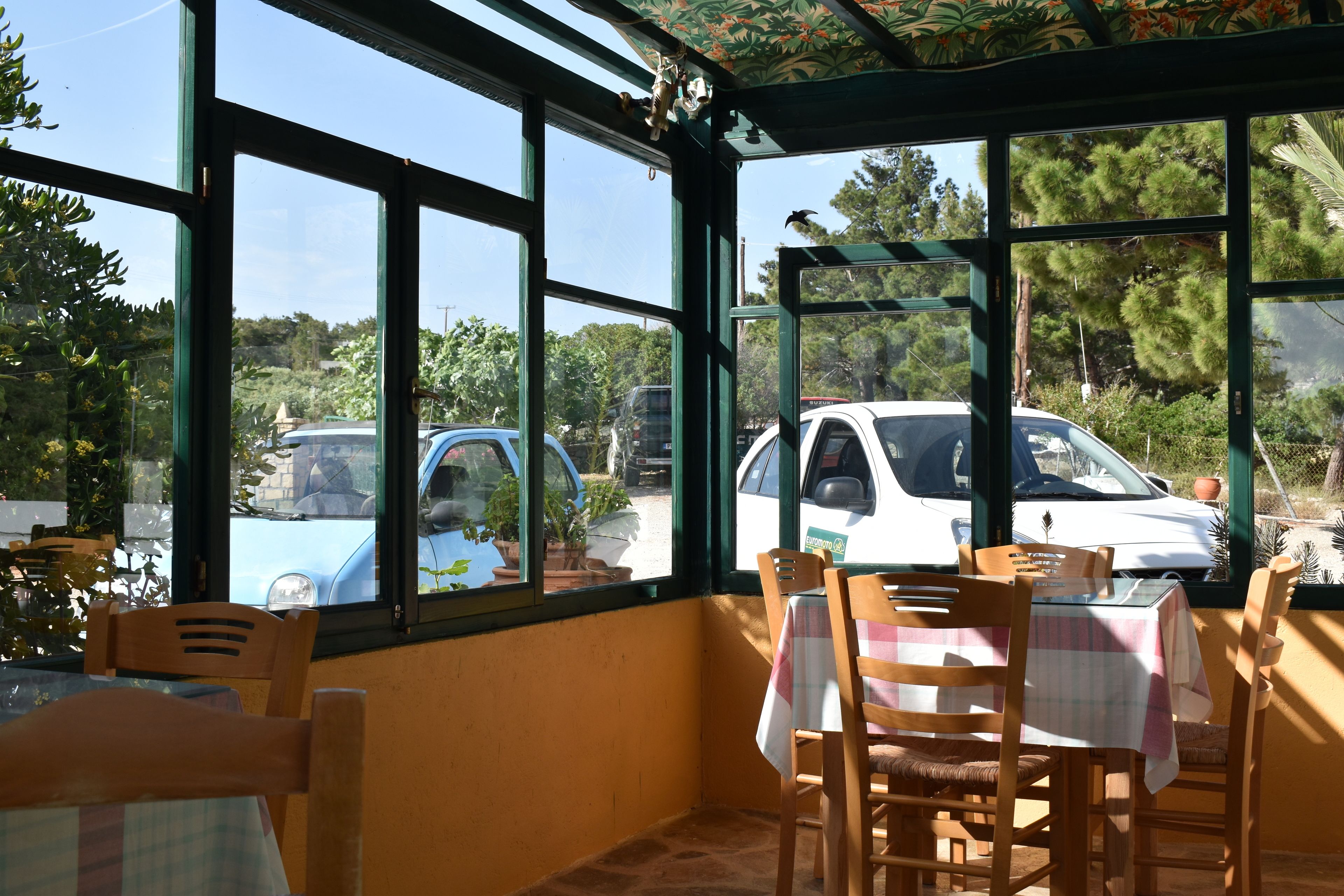 A covered patio area with large windows, wooden chairs, and a table with a checkered tablecloth.