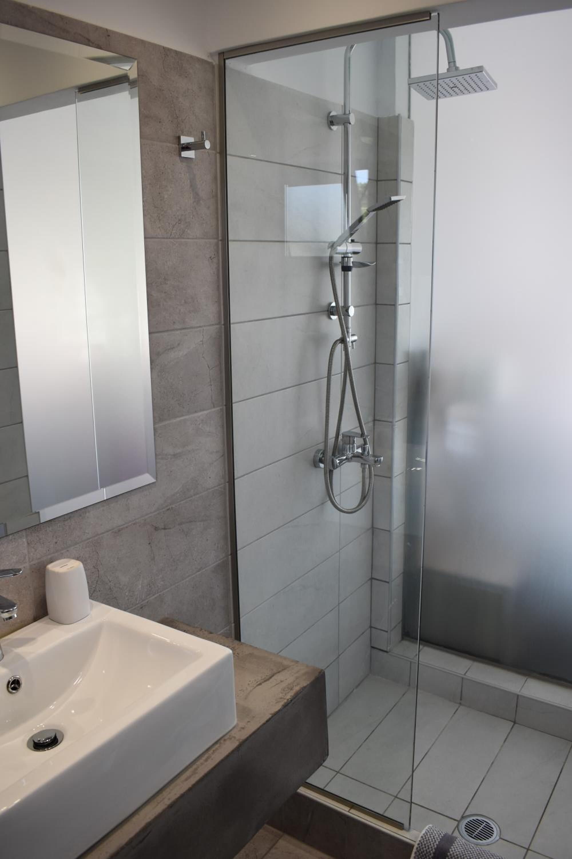 Un baño moderno con ducha de vidrio, lavamanos blanco y espejo.