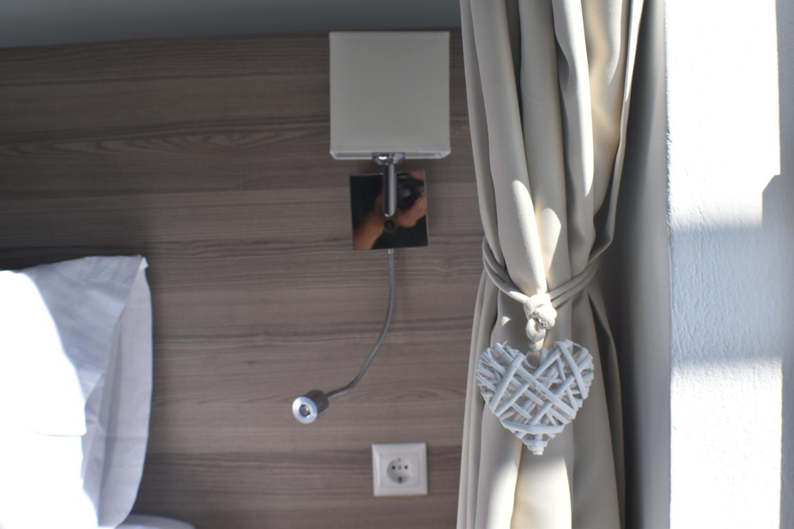 A room with a wooden headboard, a bedside lamp, a power outlet, and a curtain.