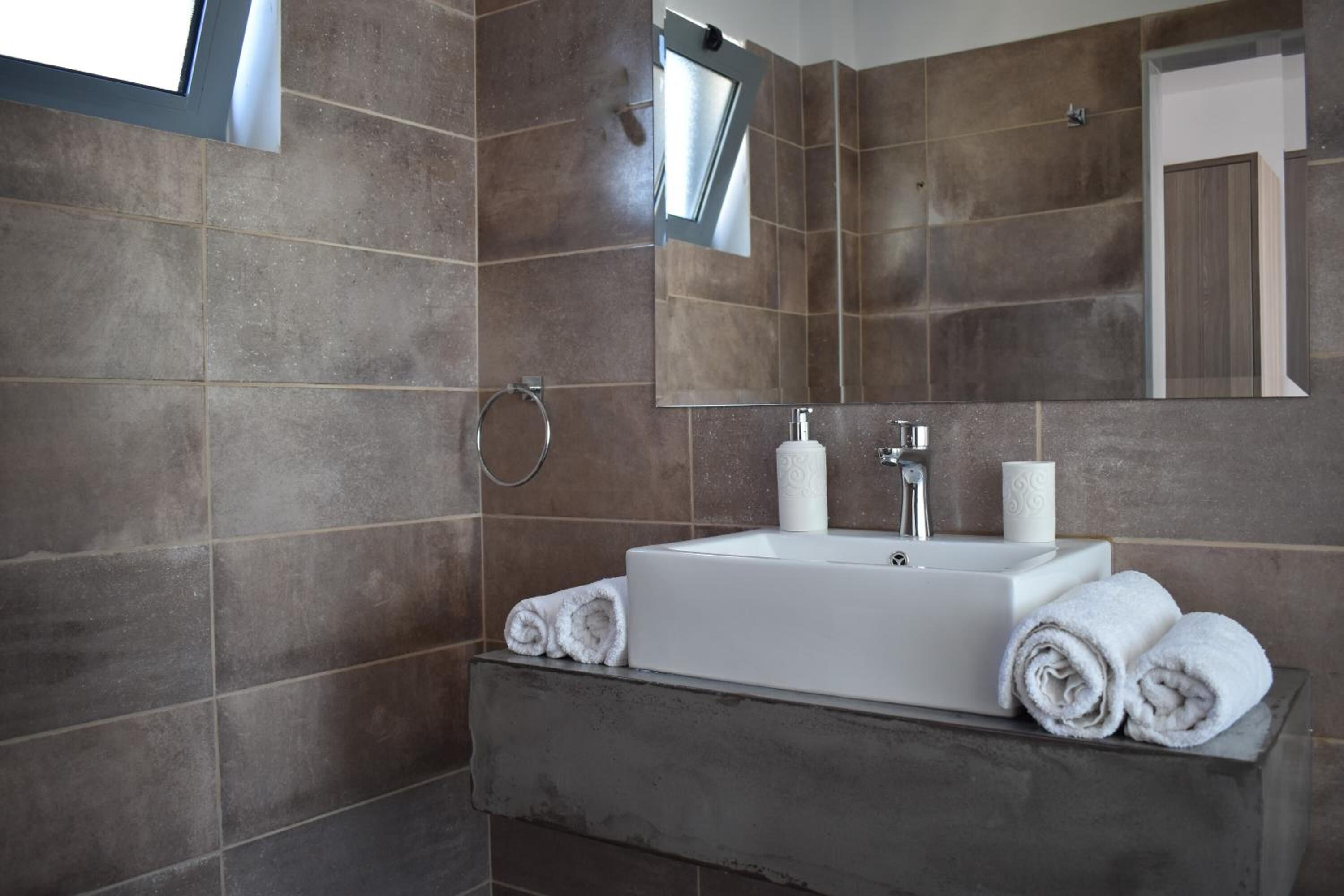 A modern bathroom with a large sink, two rolls of toilet paper, and towels neatly stacked on the counter.