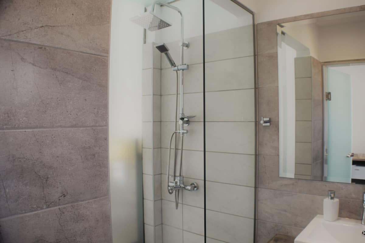 Un baño moderno con cabina de ducha de vidrio, un lavamanos blanco y un espejo grande.