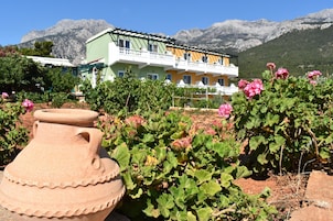 A multi-story building with balconies, surrounded by lush greenery and pink flowers.