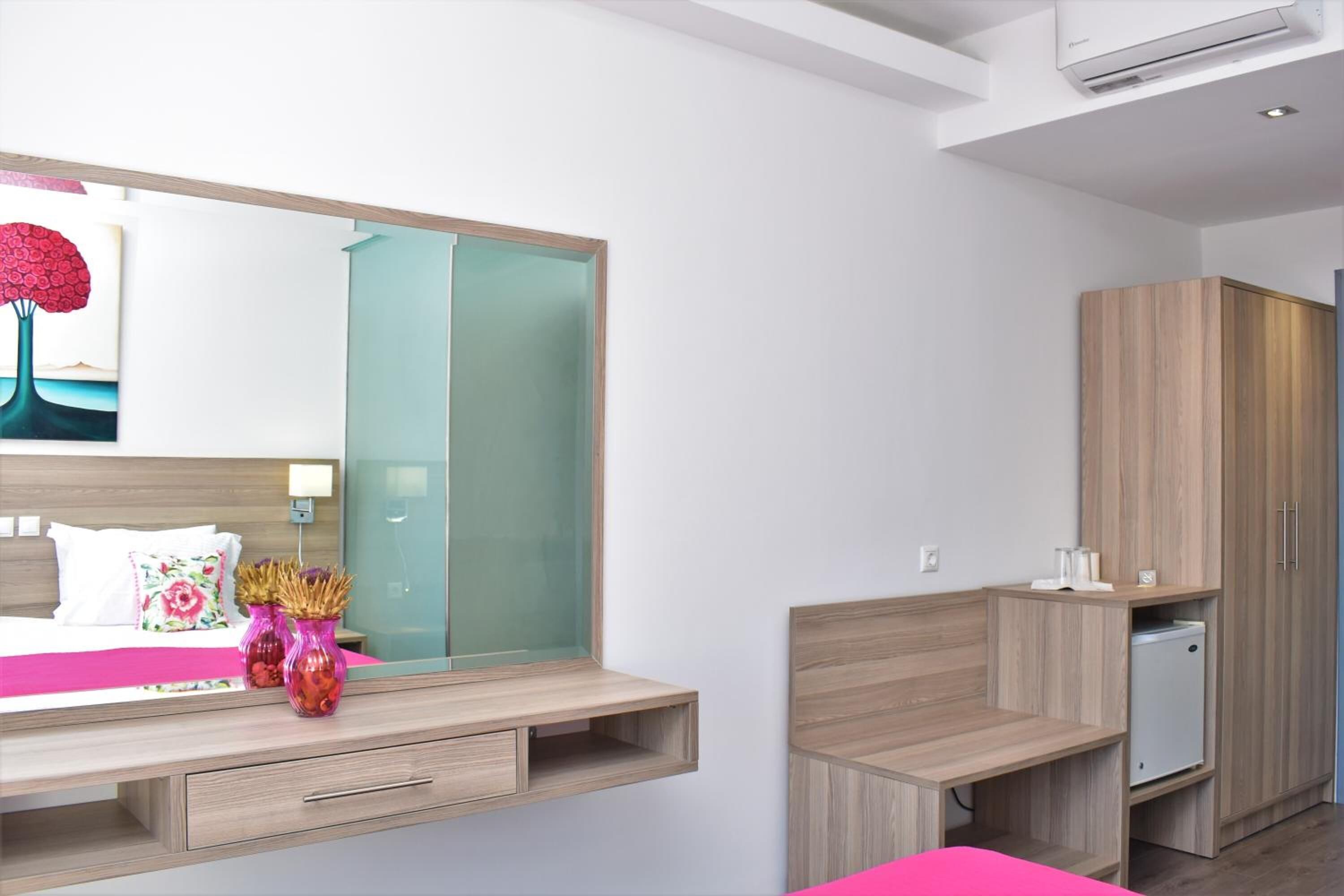 A modern bedroom with a bed, bedside table, mirror, wardrobe, and built-in mini-fridge.