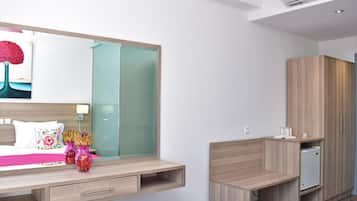 A modern bedroom with a bed, bedside table, mirror, wardrobe, and built-in mini-fridge.