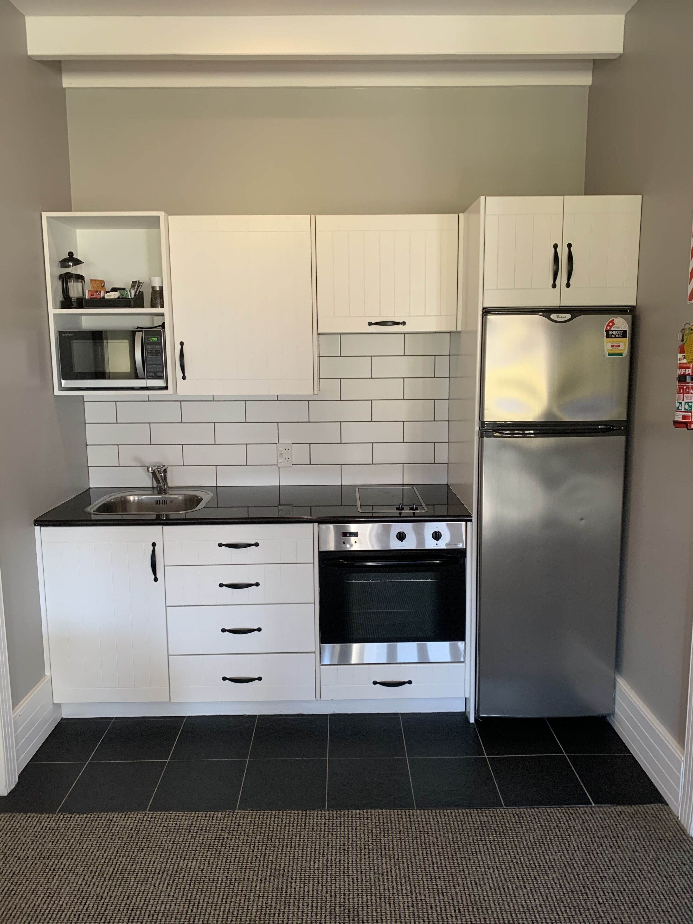 A compact kitchen with white cabinets, a stainless steel refrigerator, a microwave, and an oven.
