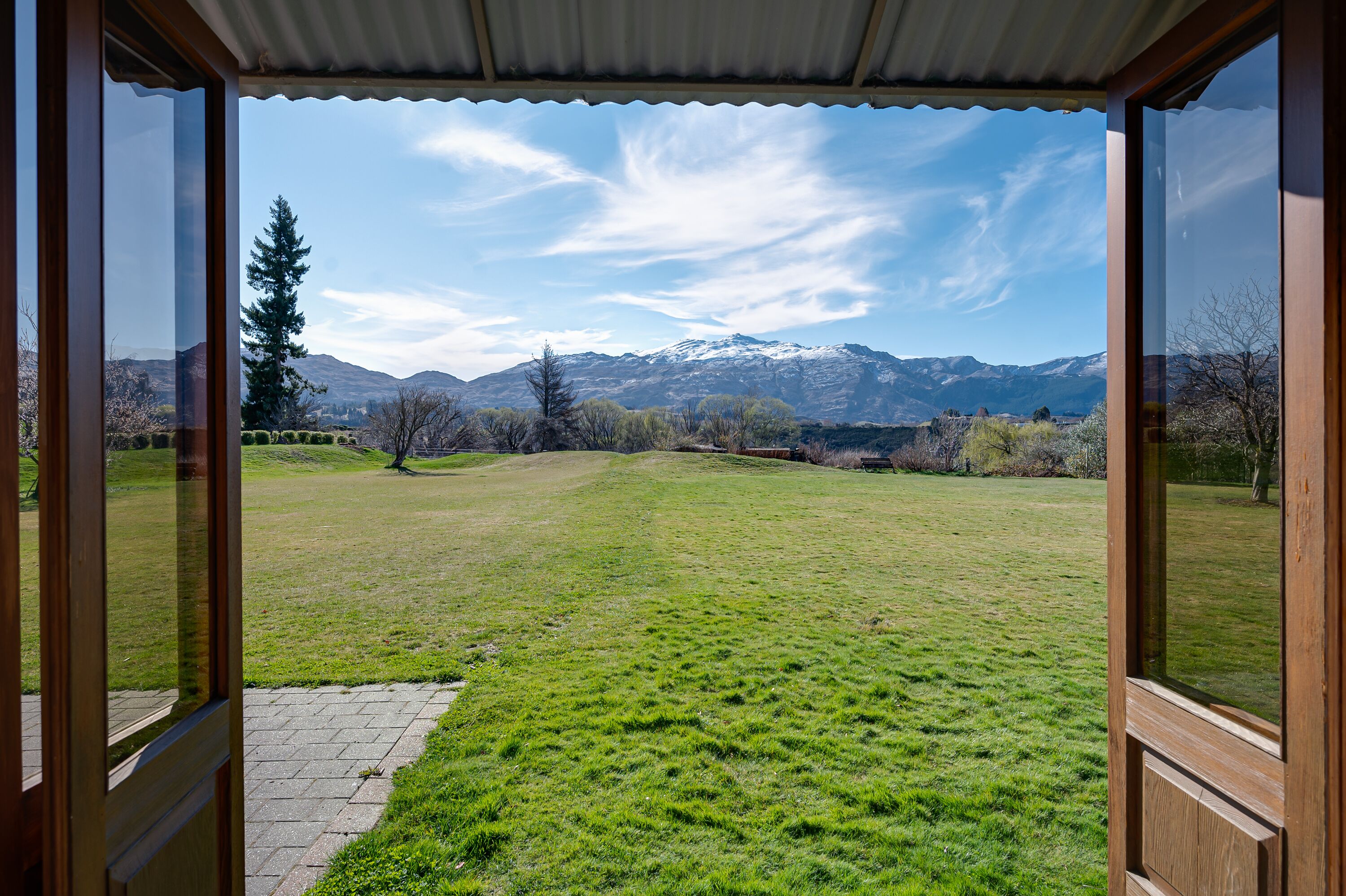 Blick aus einem Zimmer mit großen Fenstern auf ein grünes Feld und schneebedeckte Berge in der Ferne.