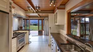 A kitchen with a large island, stainless steel appliances, and a view of the outdoors. - Manata Lodge (Lower Shotover)