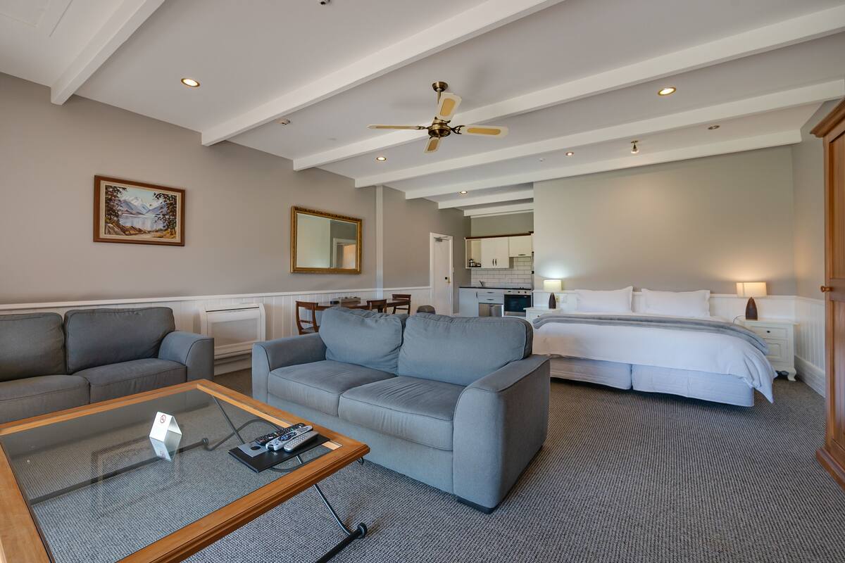 A hotel room with a large bed, a sofa, a coffee table, and a dining area.