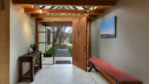 A hallway with a wooden bench, a door leading outside, and a small table with a plant. - Manata Lodge (Lower Shotover)