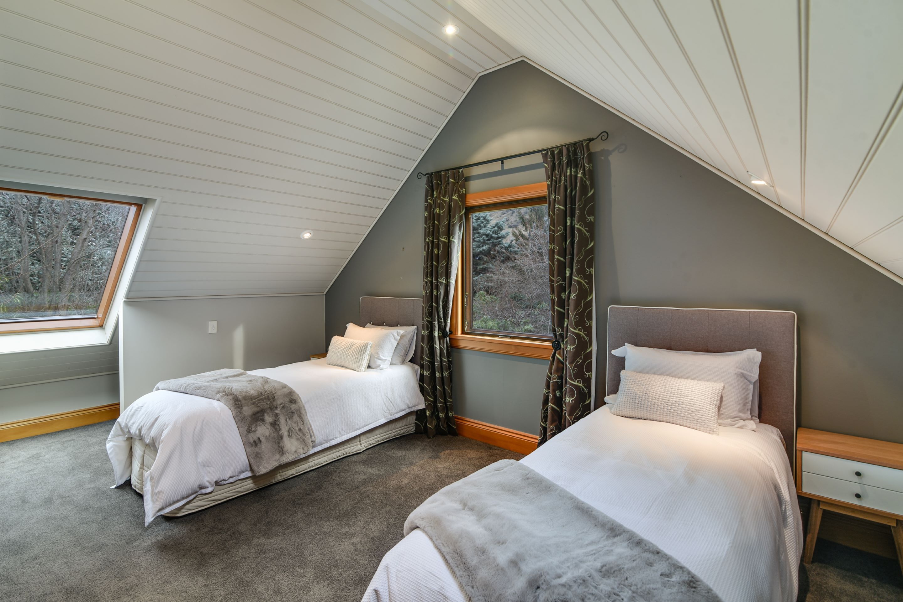 A bedroom with two beds, a skylight, and a view of trees.
