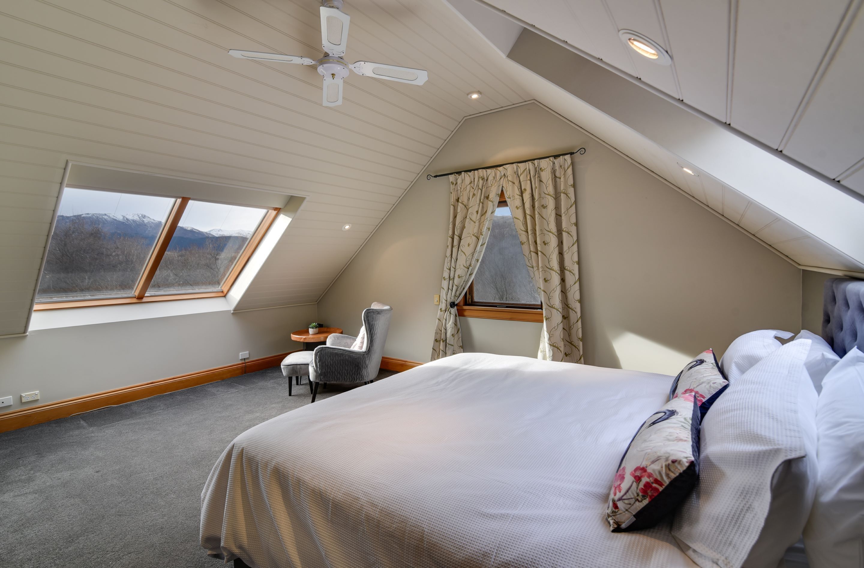 A bedroom with a large bed, a chair, a small table, and a window with curtains.