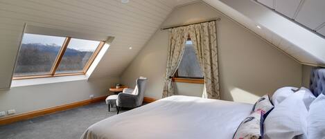 A bedroom with a large bed, a chair, a small table, and a window with curtains.