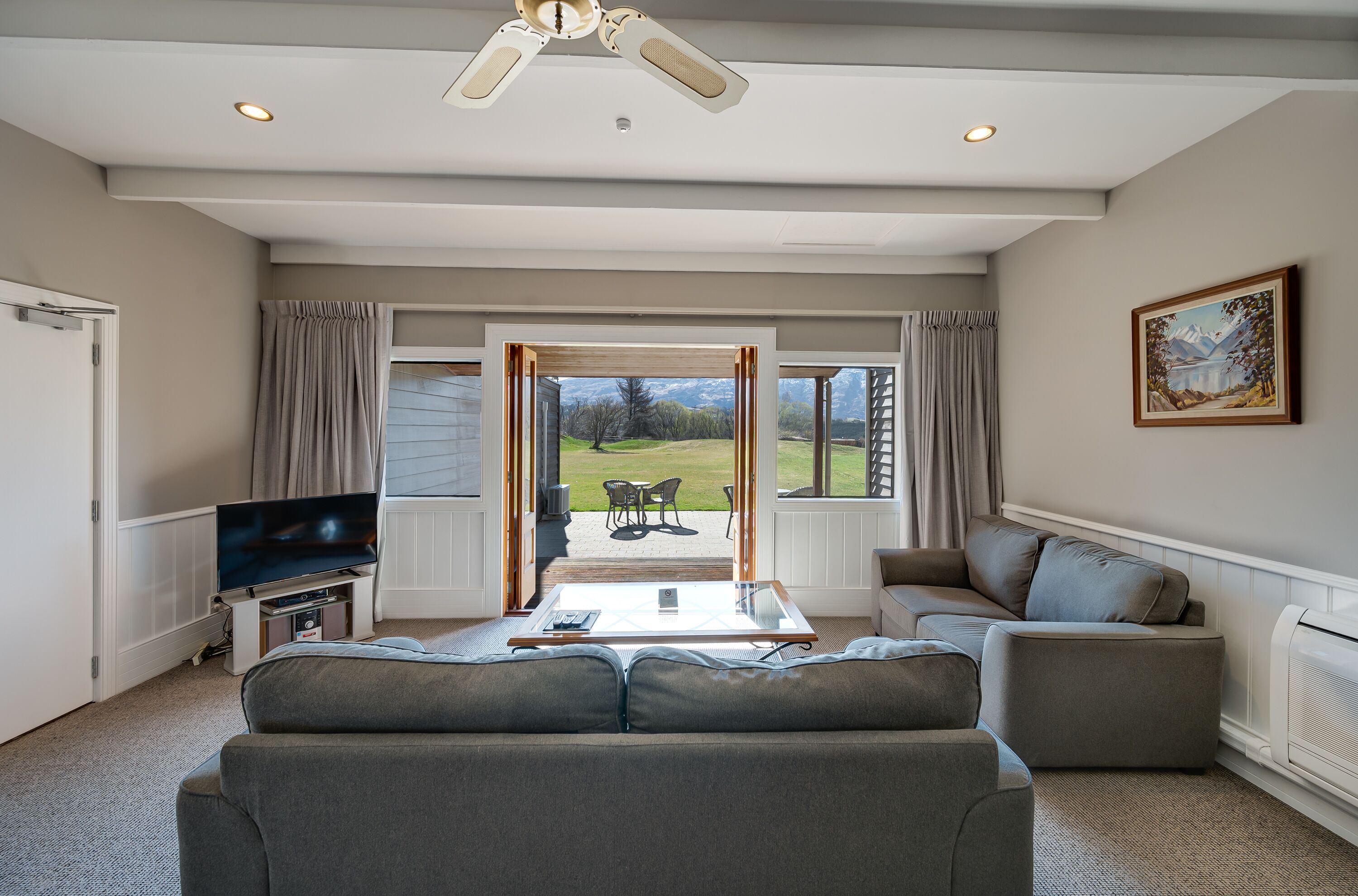 A living room with a sofa, a coffee table, a TV, and a view of a patio with outdoor furniture.