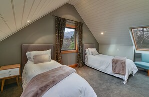 A bedroom with two beds, a window with curtains, a nightstand, and a view of mountains. - Manata Lodge (Lower Shotover)