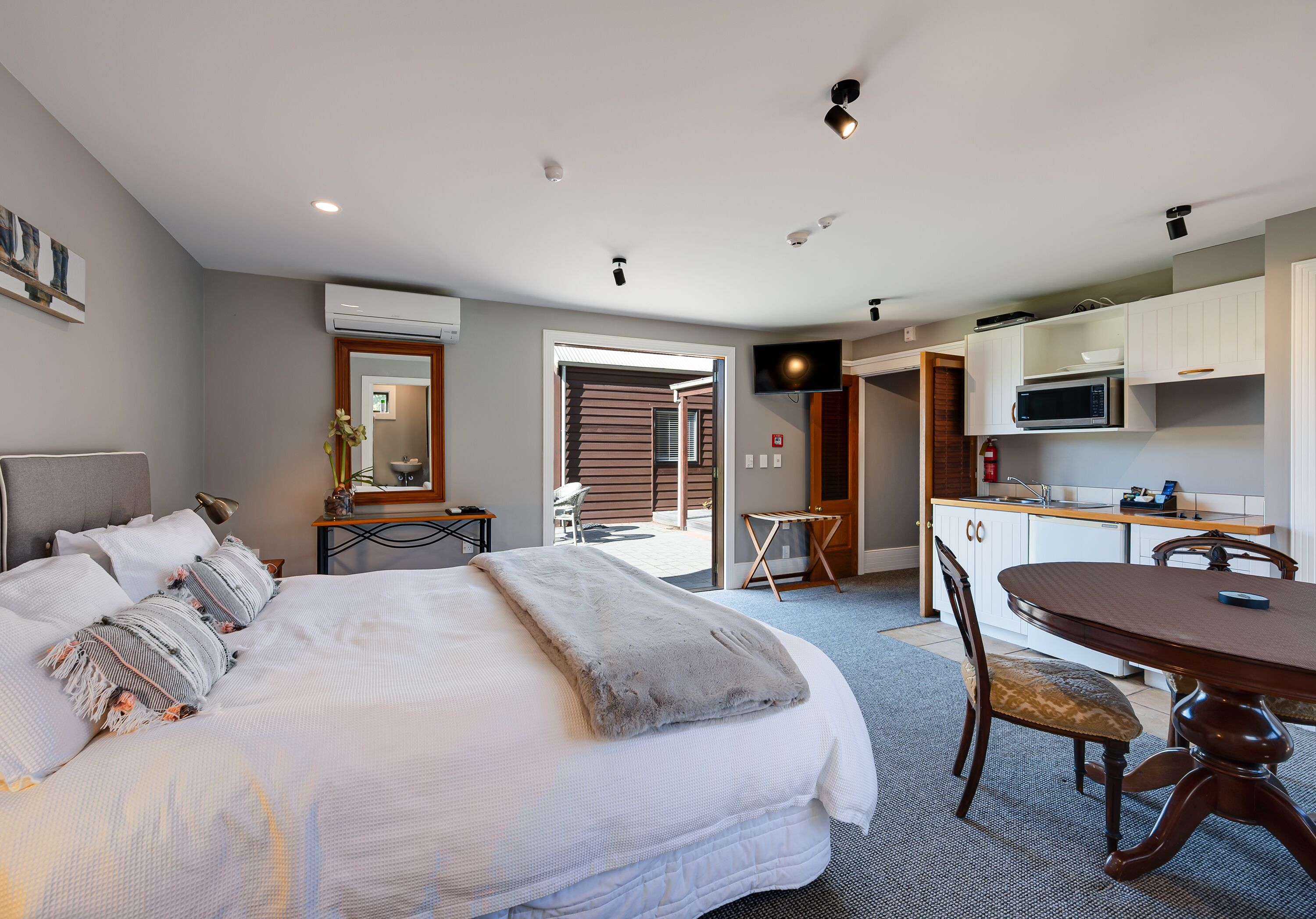A modern hotel room with a bed, a dining table, and a kitchenette.