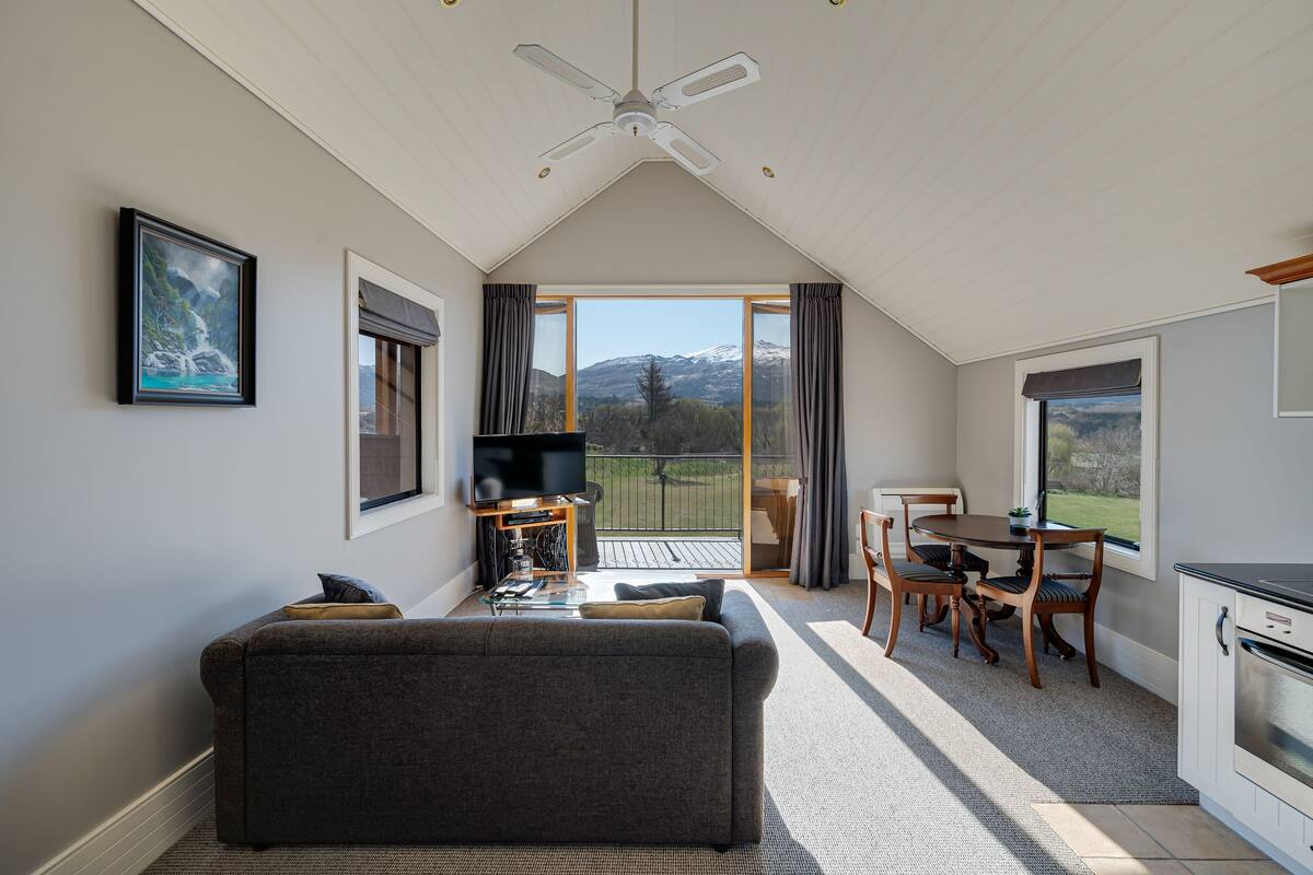A modern living room with a sofa, TV, and dining area with a view of mountains.