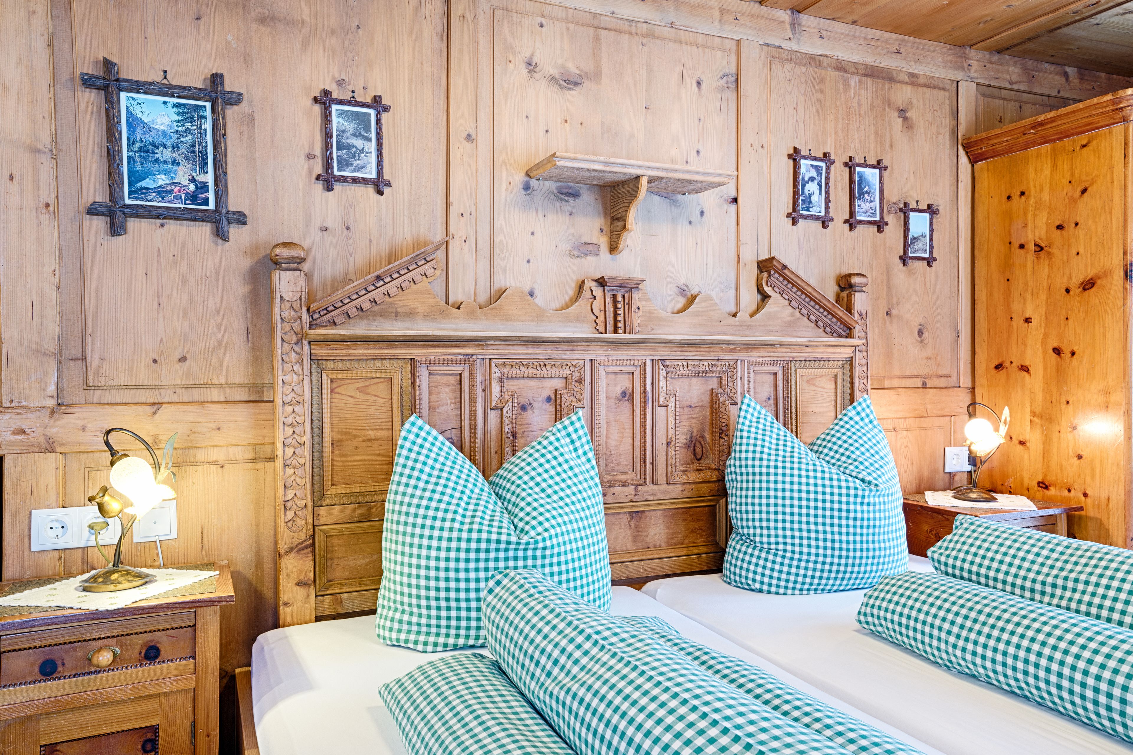 A wooden-paneled room with a bed, pillows, a nightstand, and wall-mounted pictures.