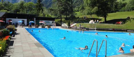 Una piscina con gente nadando y tomando el sol, rodeada de montañas y vegetación.