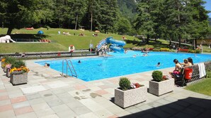 A swimming pool with a water slide, surrounded by a fence, with mountains in the background. - Landhaus Walch (Innerbraz)