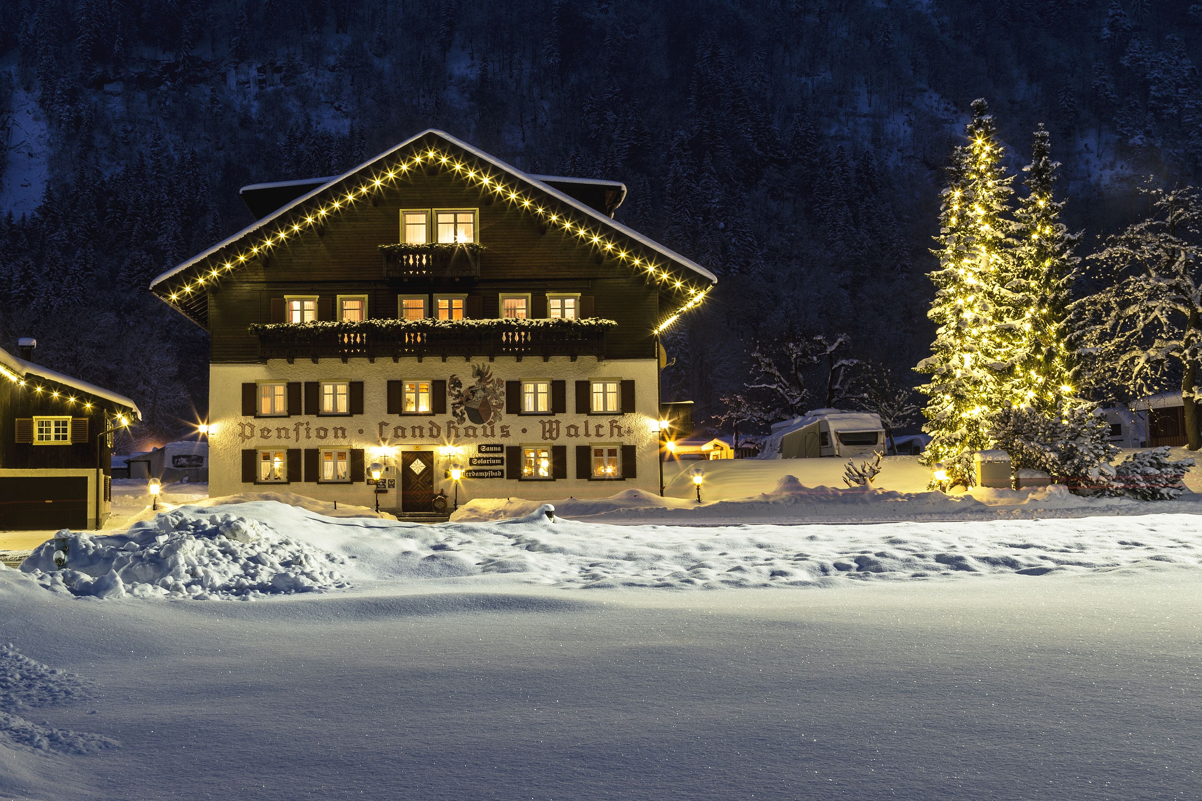 A snow-covered building with illuminated windows and a Christmas tree, surrounded by snow.