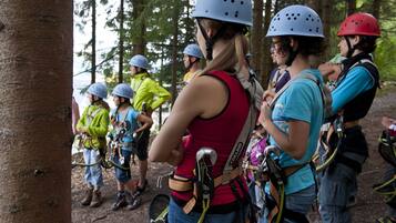 A group of people in a forested area, wearing helmets and harnesses, likely preparing for an outdoor activity.