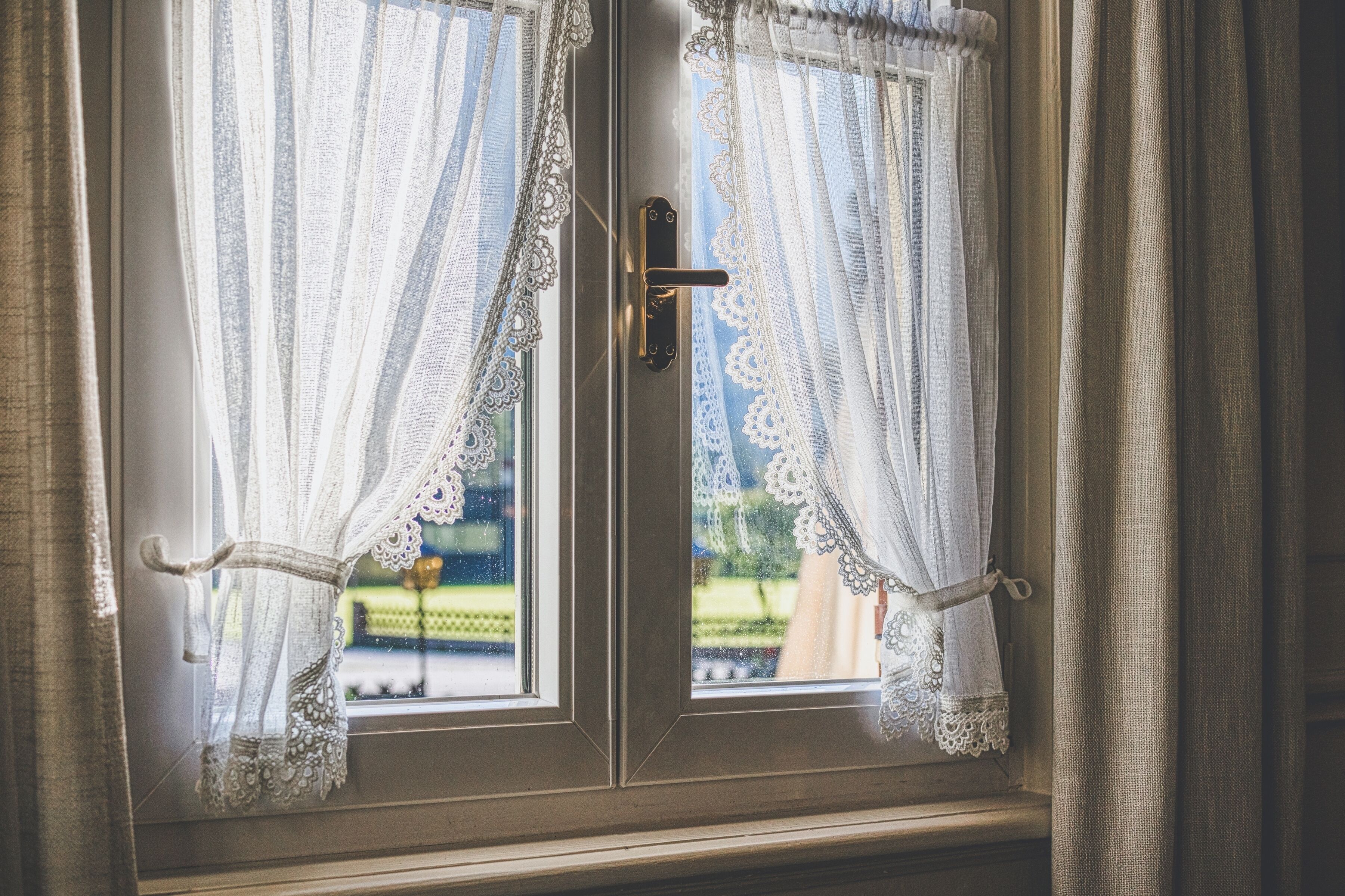 Una ventana con cortinas de encaje y un tirador de latón.
