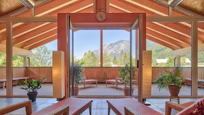 A spacious indoor area with wooden ceiling beams, large windows offering mountain views, and several wicker chairs with cushions. - Landhaus Walch (Innerbraz)