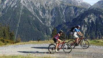Two cyclists on a gravel path with a mountainous backdrop.