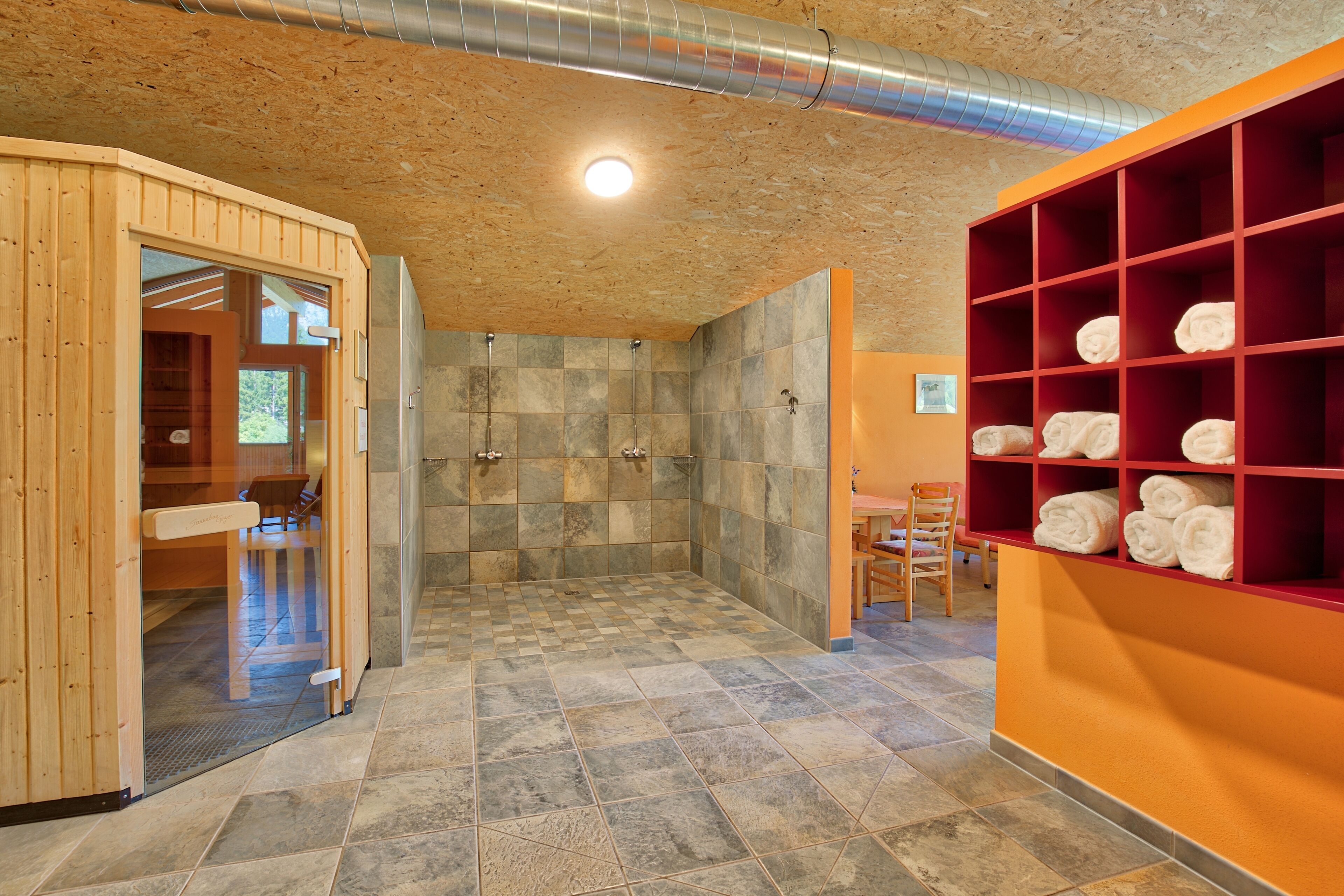A wooden sauna with a glass door, a stone shower area, and a red towel shelf.