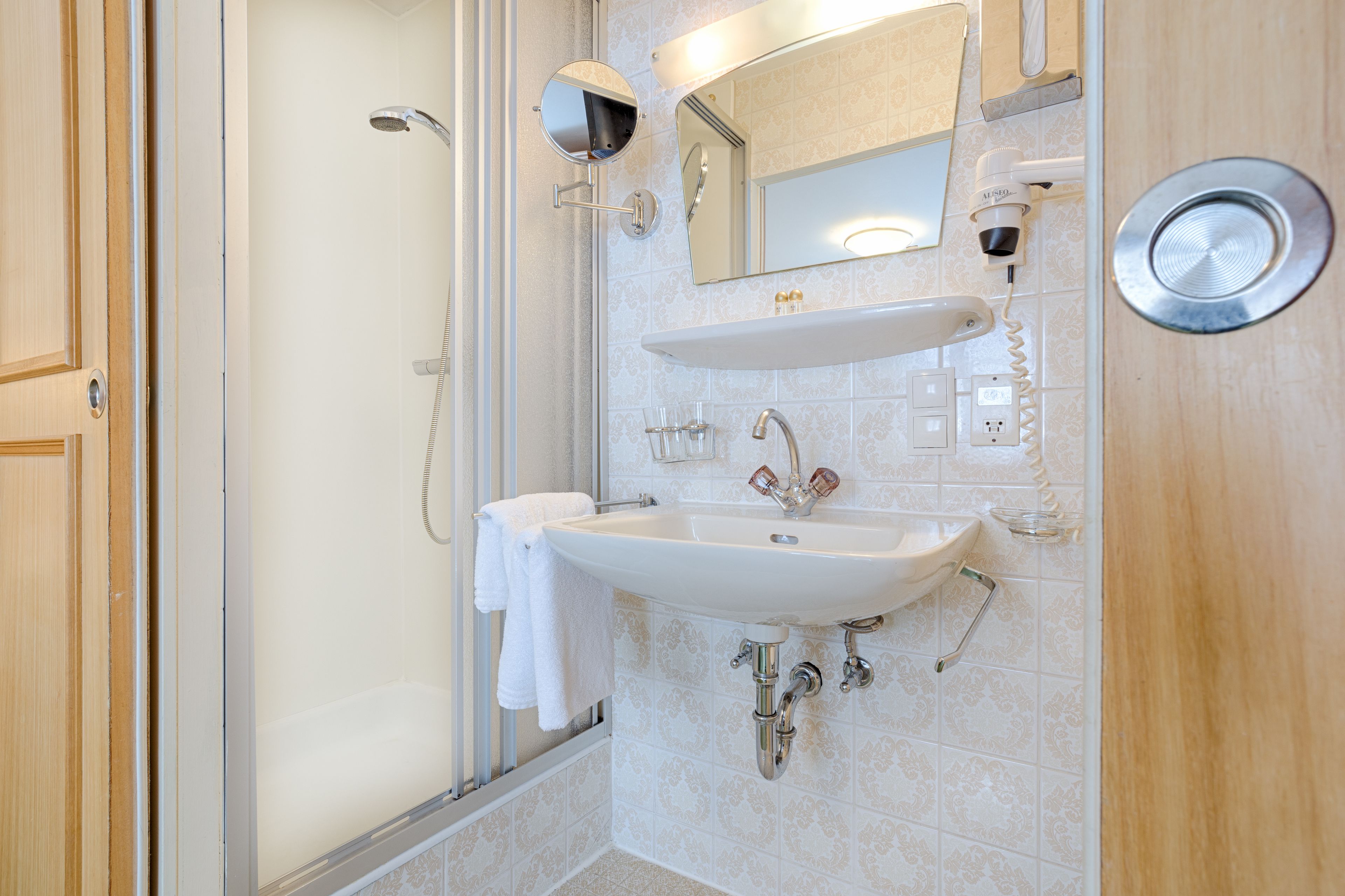 Un baño moderno con ducha de vidrio, un lavamanos blanco con espejo y una toalla colgada en la pared.