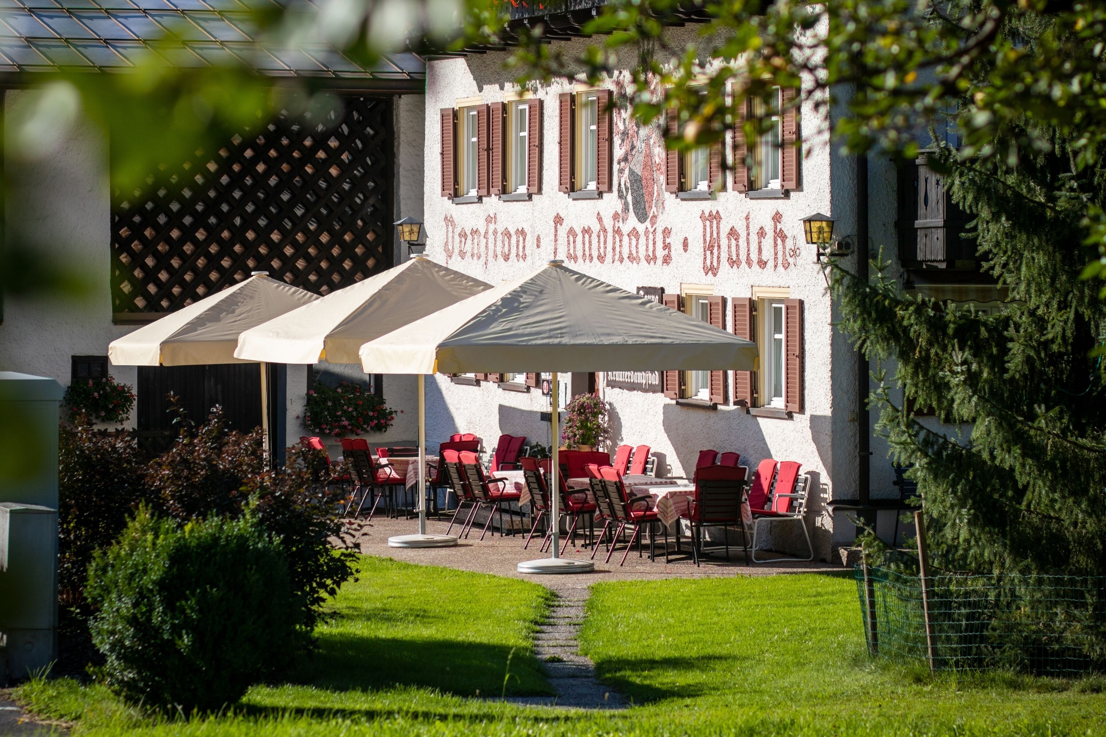 An outdoor seating area with tables and chairs, a pathway, and a building with a sign.