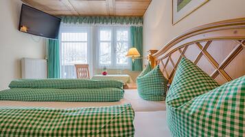 A cozy room with a checkered sofa set, a wooden headboard, a television mounted on the wall, and a window with curtains.
