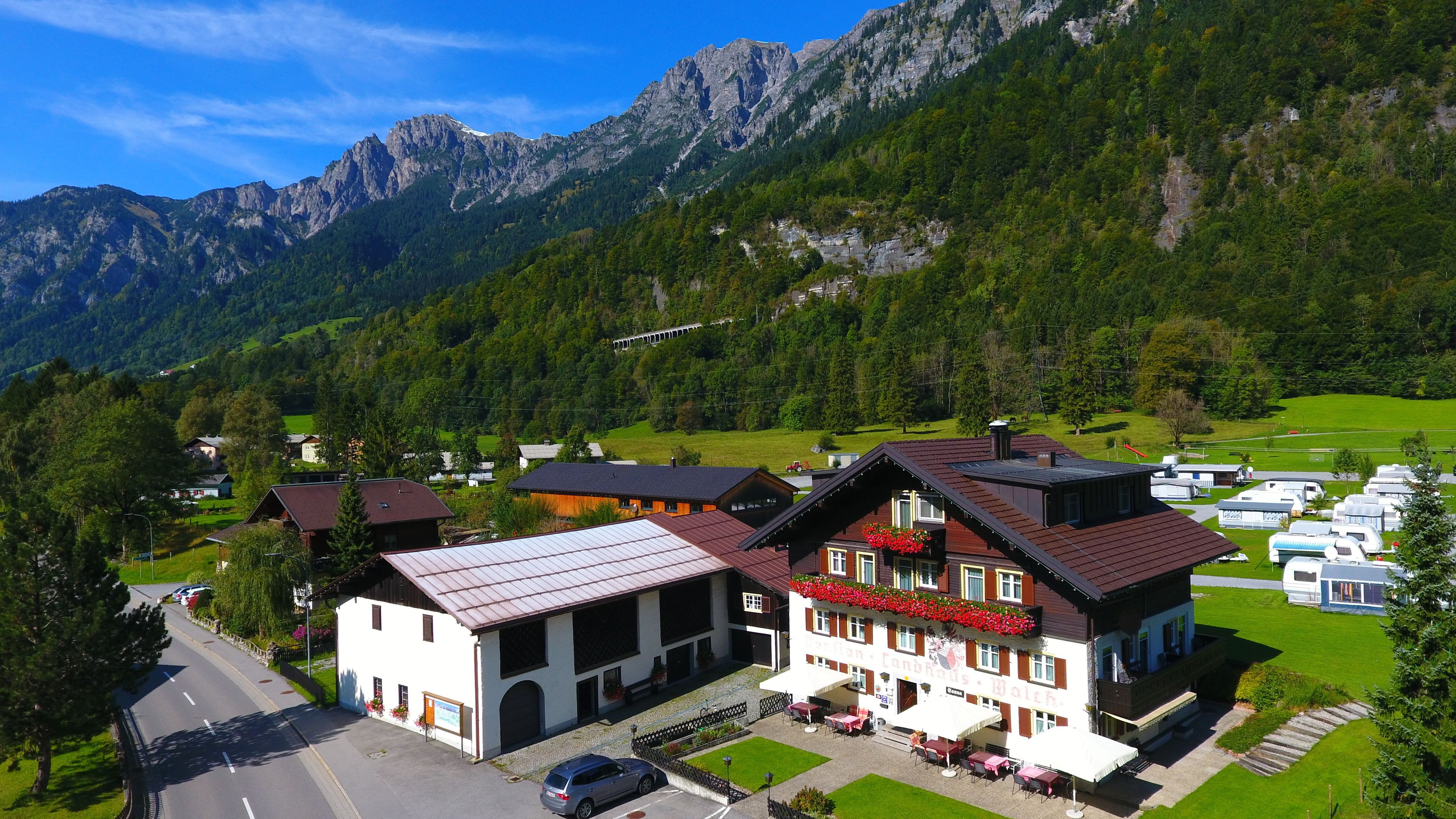 A hotel with a large patio area, a mountain backdrop, and a road in the foreground.