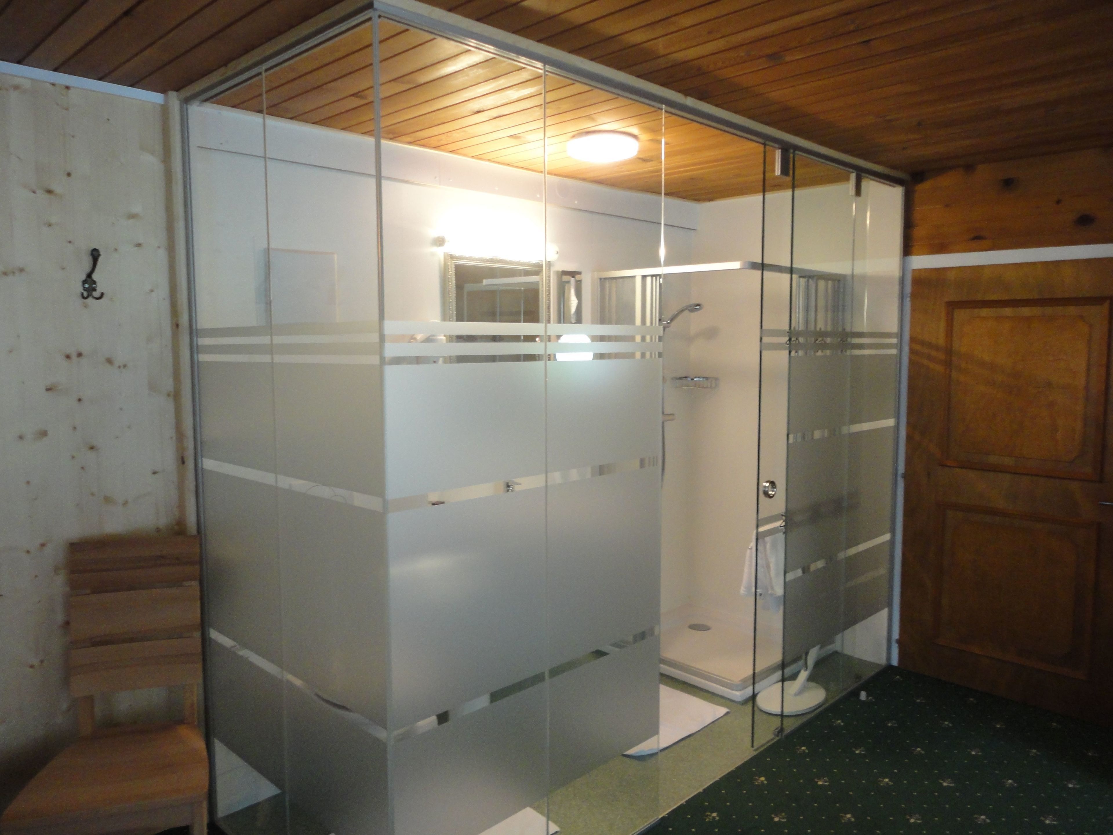 Un baño con mampara de vidrio, techo de madera y puerta de madera.