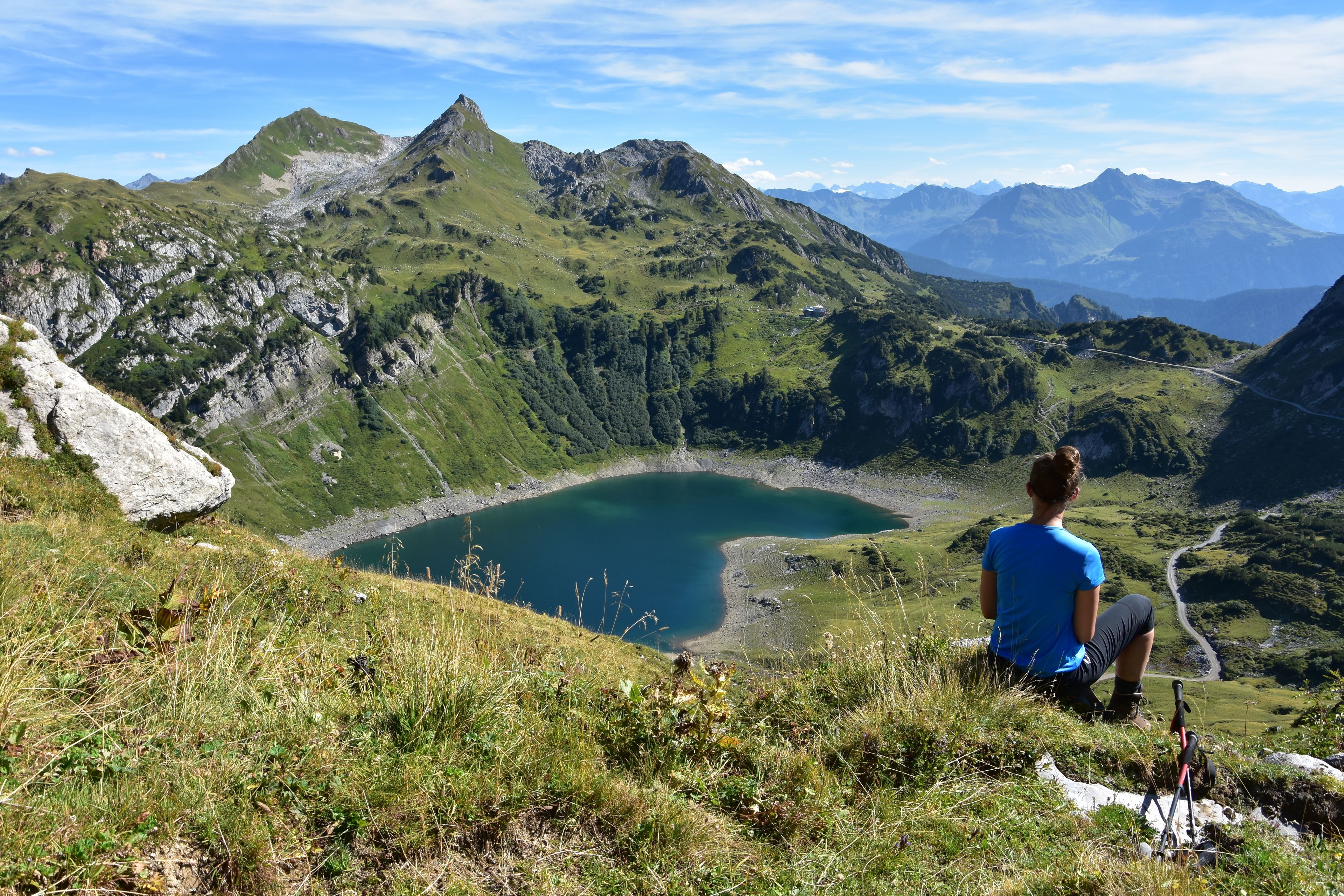 A person sitting on a grassy hill overlooking a lake with mountains in the background.
