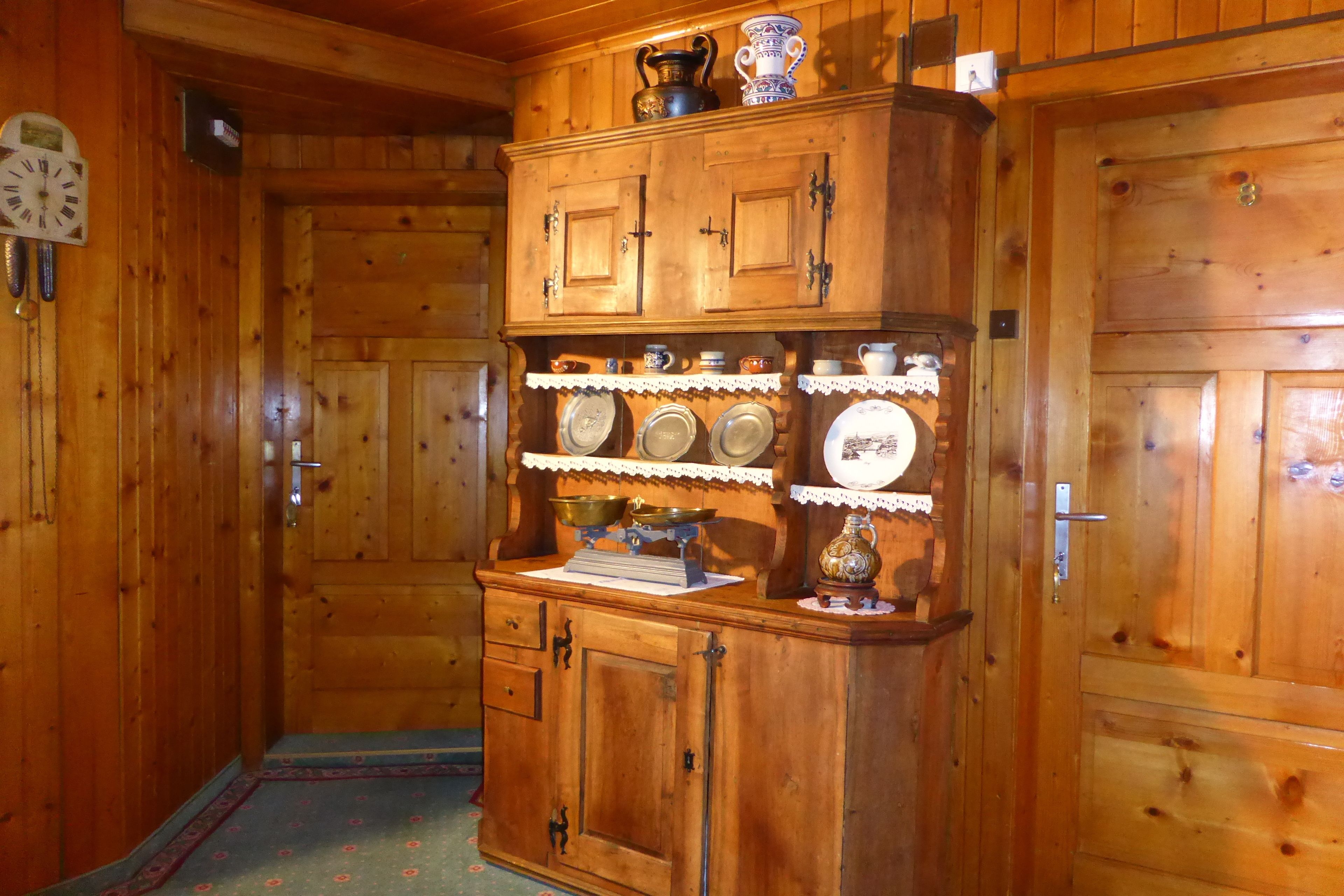 A wooden interior with a wooden cabinet containing kitchenware and a clock.