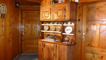 A wooden interior with a wooden cabinet containing kitchenware and a clock.