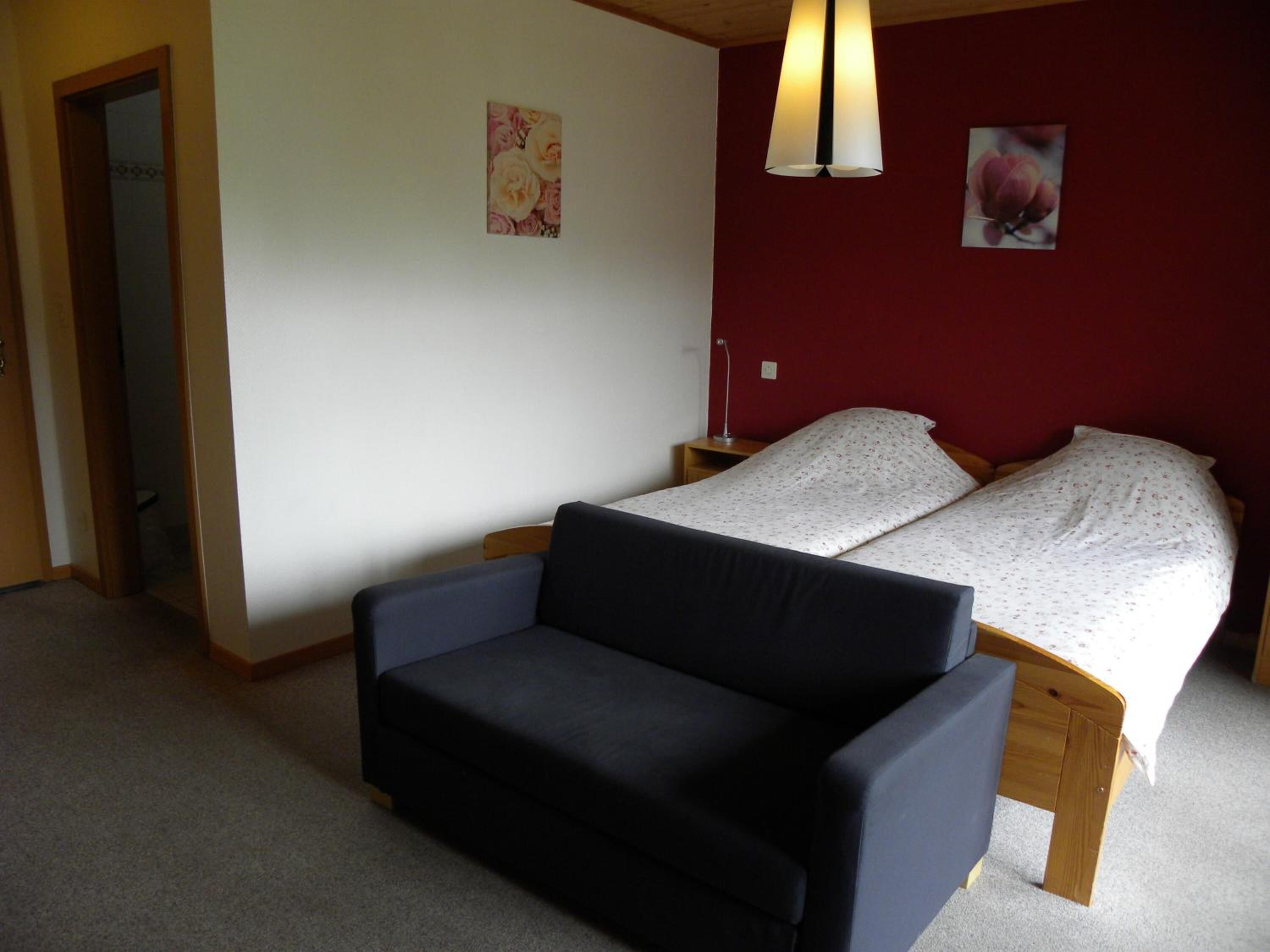 A bedroom with a bed, a sofa, and two wall-mounted lamps.
